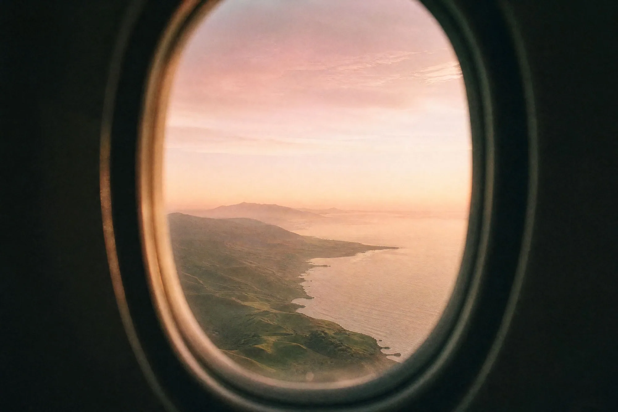 View through an airplane window over a green coastline at sunrise