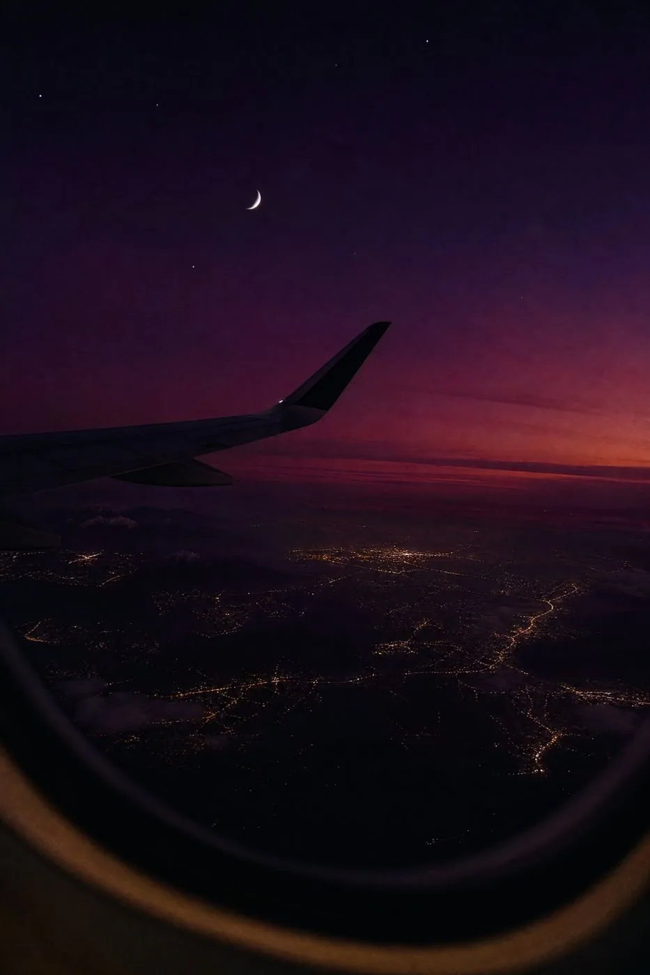 Night flight: wing, crescent moon and city lights
